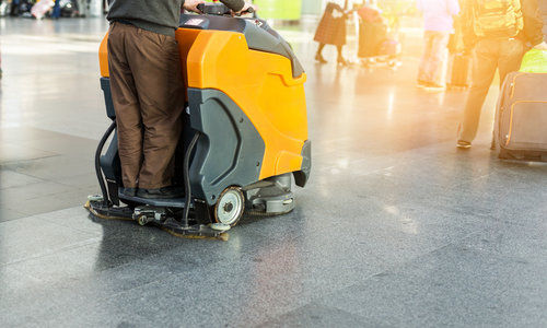 Man driving professional floor cleaning machine at airport or railway station.