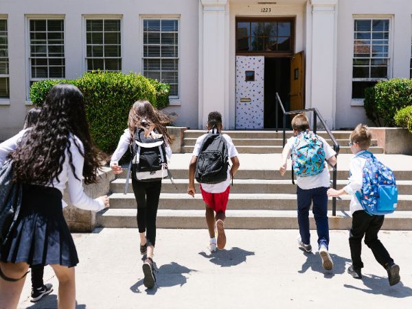 Group of students with backpacks running into school, captured from behind, showing excitement