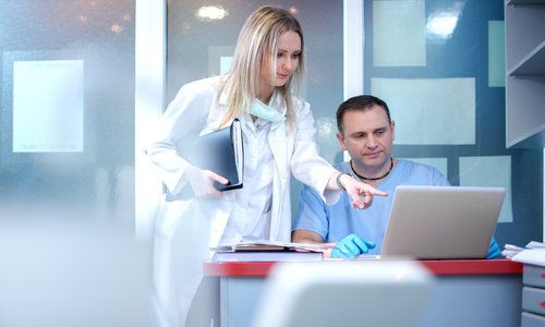 Nurse and doctor using laptop in medical clinic.