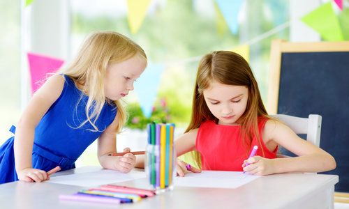 Two Cute Little Sisters Drawing with Colorful Pencils at a Daycare