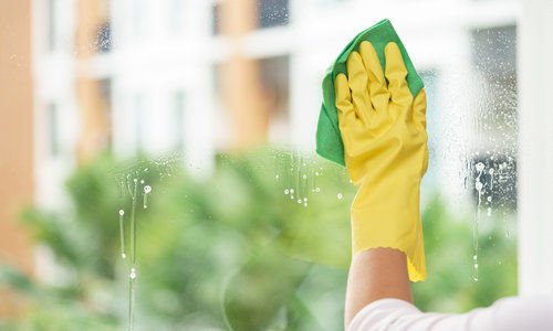 Woman housekeeper cleaning the mirror with green cloth.