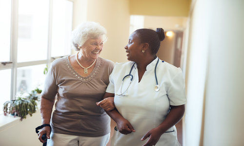 Senior Woman Walking in the Nursing Home Supported by a Caregiver.